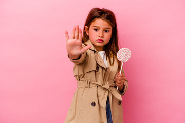 Little caucasian girl holding a lollipop isolated on pink background standing with outstretched...