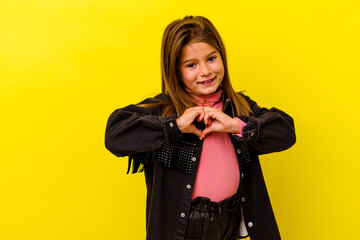 Little caucasian girl isolated on yellow background smiling and showing a heart shape with hands.