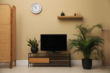 Modern TV on cabinet and green plants near beige wall in room. Interior design