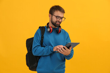 Student with headphones and backpack using tablet on yellow background