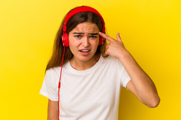 Young caucasian woman listening to music isolated on yellow background showing a disappointment gesture with forefinger.