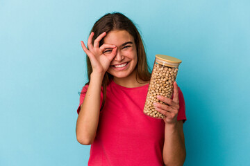 Young caucasian man holding chickpeas jar isolated on white background excited keeping ok gesture...