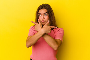 Young caucasian woman isolated on yellow background points sideways, is trying to choose between two options.