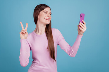 Photo of excited cheerful girl make selfie smartphone show peace cool v-sign isolated over blue color background