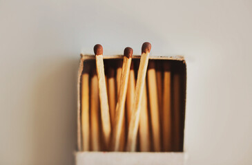 In a simple cardboard matchbox there are wooden matches with brown sulfur heads. Household items. Flammable objects. Macro. Three matches stick out of the box.