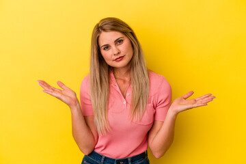 Young russian woman isolated on yellow background doubting and shrugging shoulders in questioning gesture.