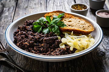 Fried blood sausage with onion and toasted bread on wooden table
