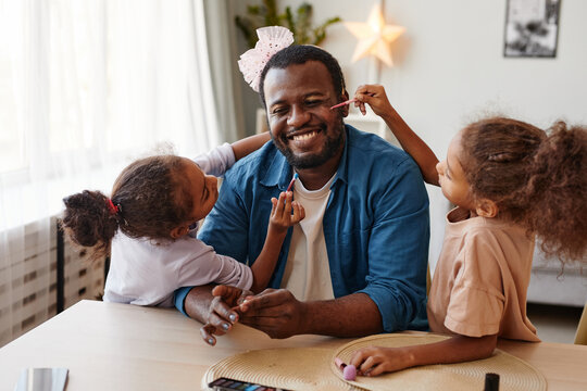 Portrait of happy African-American father playing with daughters at home and doing makeup