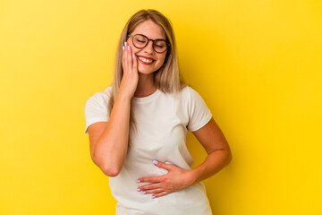 Young russian woman isolated on yellow background laughs happily and has fun keeping hands on...