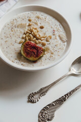 Oatmeal porridge with pomegranate, apples, oranges, pine nuts, walnuts, in a white bowl and silver spoons. Top view. Healthy breakfast.