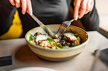 Young woman hand eating donburi with chicken and rice using knife and fork fom bowl