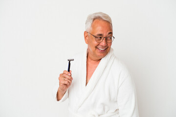 Senior american man wearing bathrobe holding razor blade isolated on white background looks aside smiling, cheerful and pleasant.