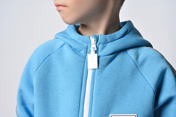 Closeup of kid boy in blue jumpsuit or hoodie with zipper standing with head turned, looking aside...