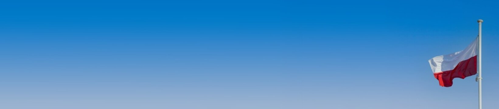 Polish flag flying in the wind on a high mast against the background of blue sky. Panorama. © fotodrobik