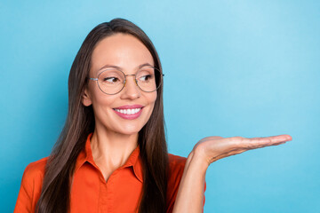 Photo of sweet charming mature lady dressed red shirt glasses looking holding arm empty space smiling isolated blue color background