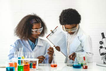 Two african american cute little boy and girl student child learning research and doing a chemical experiment while making analyzing and mixing liquid in test tube at science class on the table