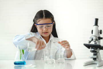 Fototapeta premium Cute little girl student child learning research and doing a chemical experiment while making analyzing and mixing liquid in glass at science class in school.Education and science concept