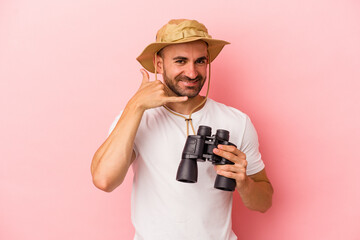 Young caucasian bald man holding binoculars isolated on pink background  showing a mobile phone call gesture with fingers.