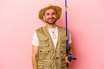 Fototapeta premium Young bald fisherman holding a rod isolated on pink background happy, smiling and cheerful.