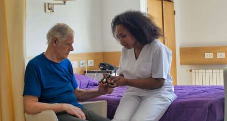 African female doctor visiting elderly male patient in hospital bed. Rehabilitation and retirement concept