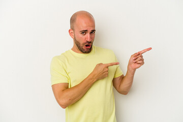 Young bald man isolated on white background pointing with forefingers to a copy space, expressing excitement and desire.