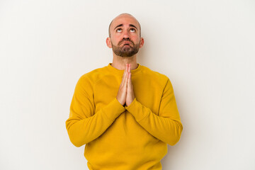 Young bald man isolated on white background holding hands in pray near mouth, feels confident.