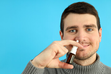 Young man with nasal spray on blue background, runny nose concept