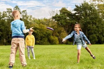 childhood, leisure and people concept - group of happy children playing game with flying disc at...