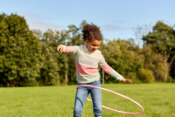 childhood, leisure and people concept - happy african american girl playing with hula hoop at park