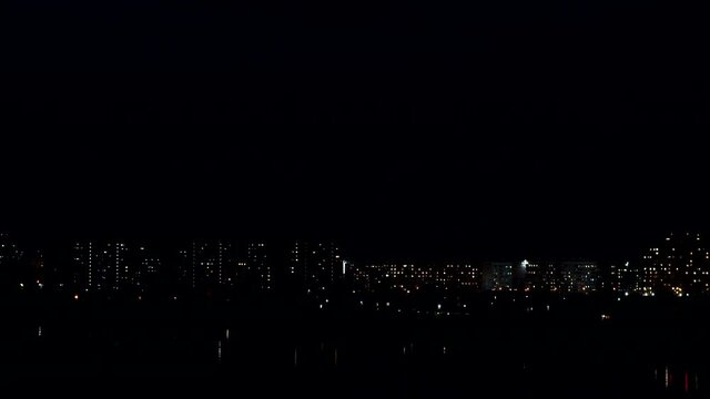 Night time of illuminated city with high-rise buildings and offices under dark blue and black sky without stars time-lapse