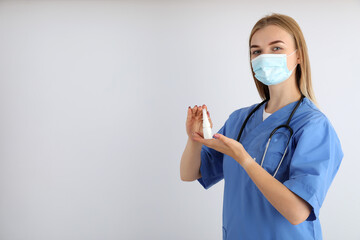 Young nurse with nasal spray on light background, seasonal cold treatment