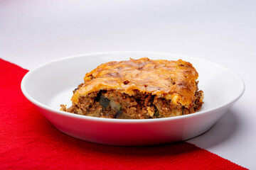 studio shot of homemade musaka on a white plate with a red and white background