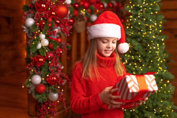 Happy child in a Santa red hat is holding Christmas gift with smile. Christmas concept.