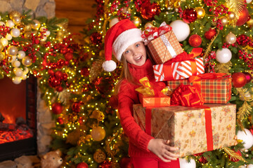 Happy child in a Santa red hat is holding lots of Christmas gifts with smile. Christmas concept.
