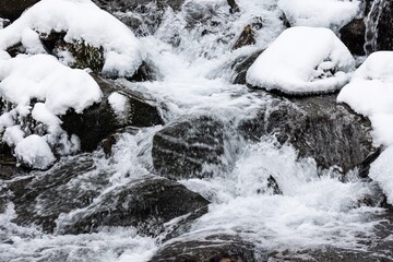 Small waterfall of cold water flow among the stones covered with snow