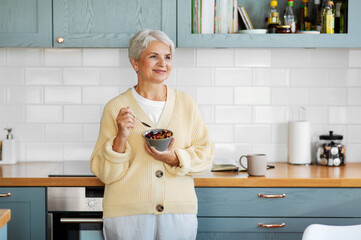 breakfast, food and people concept - happy smiling woman with spoon eating cereal on kitchen at home