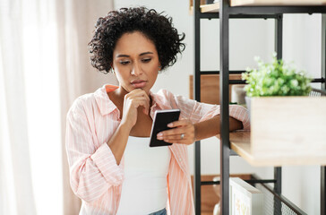 technology and people concept - woman with smartphone standing at shelf at home