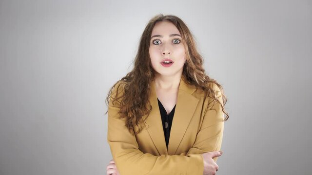Isolated portrait of woman shocked by some news who is closing her mouth by hand. A serious young lady is standing on white background and suddenly getting amazed by unbelievable information