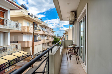 Standard narrow balcony of apartment located in the town center, with outdoor furniture table and two chairs, with the view to other buildings and street.
