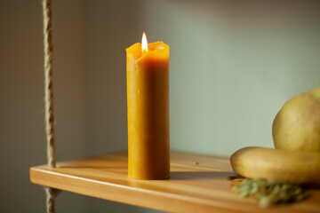 The candle burns during the day. A wax candle is on a shelf.