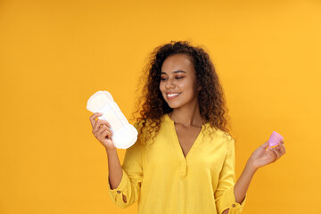 Young African American woman with menstrual cup and pad on yellow background