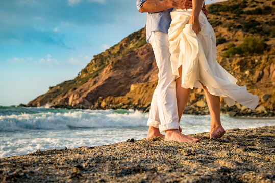 Close up legs photo. Couple in love standing on the sandy beach with the sea at the blurred background. 