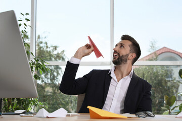 Handsome businessman playing with paper plane at desk in office