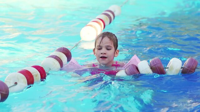a funny little girl swims in inflatable armbands in a pool near the buoys. 