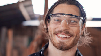 Portrait of Caucasian male carpenter wearing protective glasses looking smile at camera. happy craftsman at the workshop studio