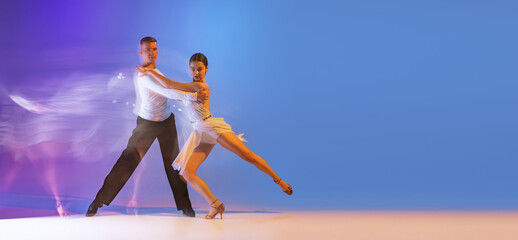 Two young graceful dancers, flexible man and woman dancing ballroom dance isolated on gradient blue...