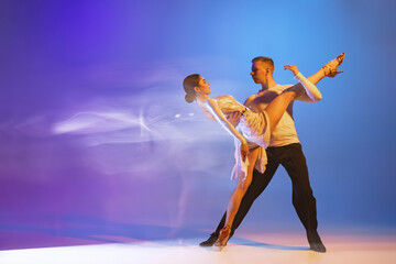 Fototapeta na wymiar Young graceful dancers, flexible man and woman dancing ballroom dance isolated on gradient blue purple background in neon mixed light