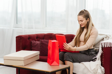 Young excited woman is unboxing her parcel, ordered online by internet, while sitting on the sofa