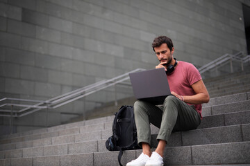 Handsome man working with laptop on city street. Man using his laptop while sitting on stairs outdoors.