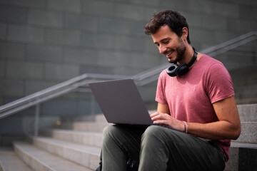 Handsome man working with laptop on city street. Man using his laptop while sitting on stairs outdoors.